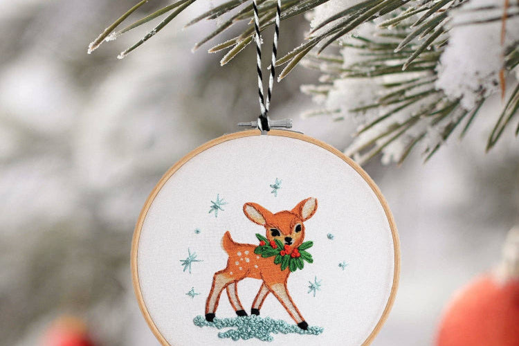 Embroidered deer ornament on a Christmas tree with snow and ornaments in the background